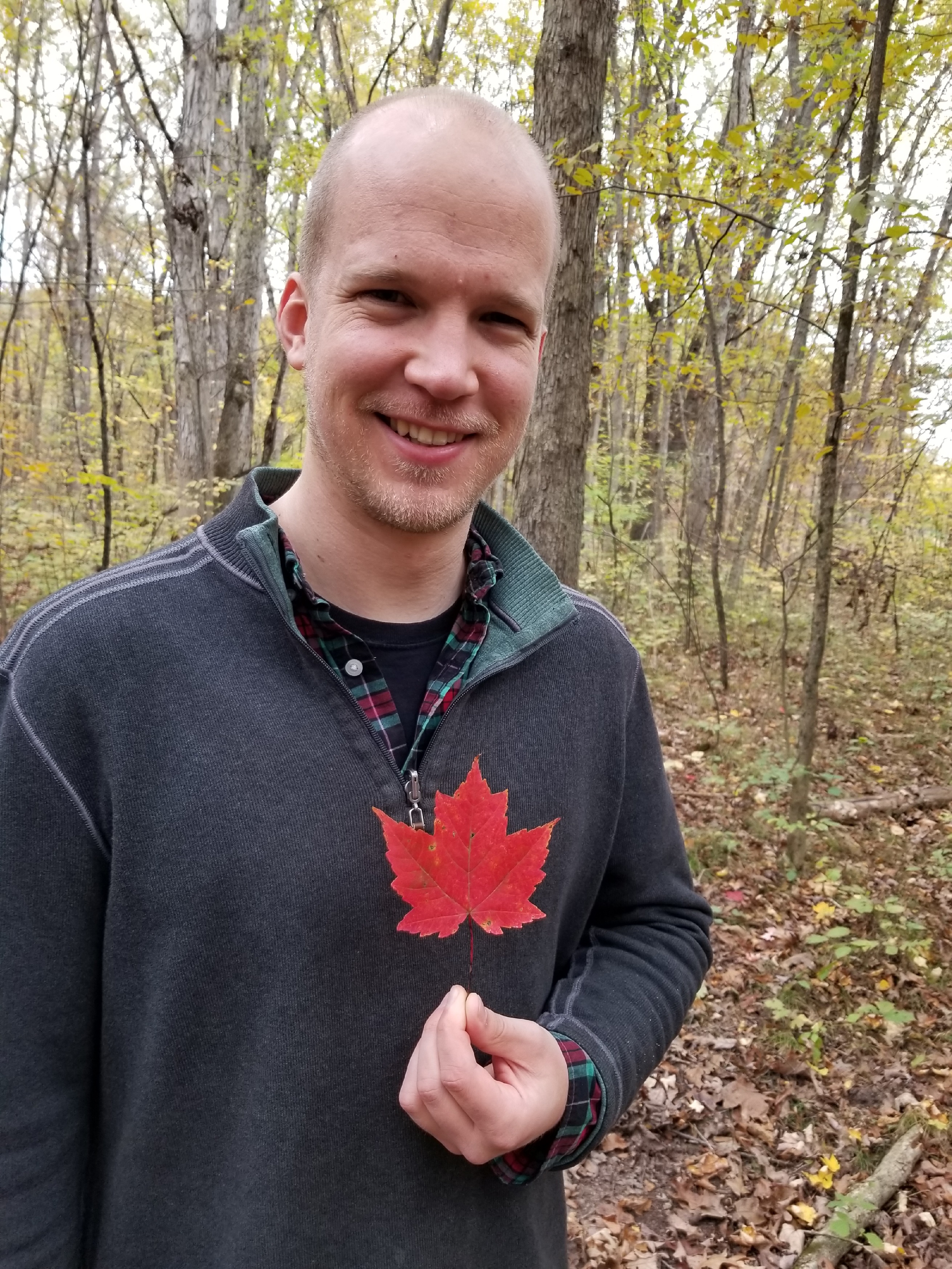Greg Bodwin holding a red maple leaf in the woods.